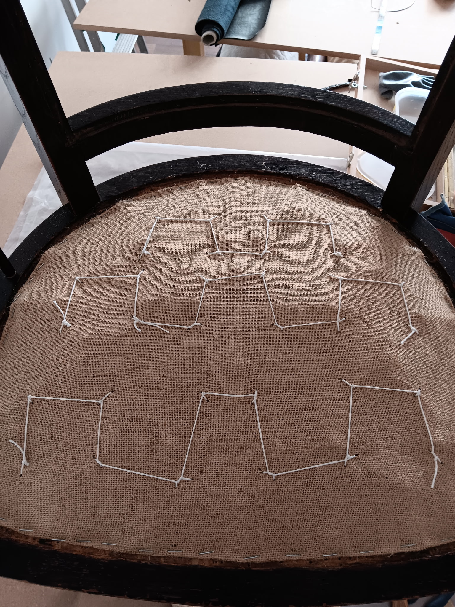 La toile de jute tendue sur l’assise du fauteuil, avec les points qui fixent les ressorts